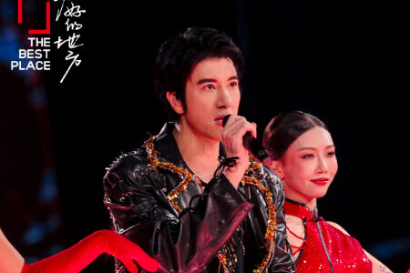 Wang Leehom performing with a female co-performer in traditional red dress, both holding microphones on stage