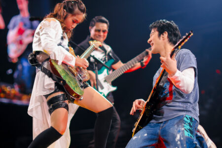 Wang Leehom playing electric guitar alongside a female guitarist in an energetic concert performance